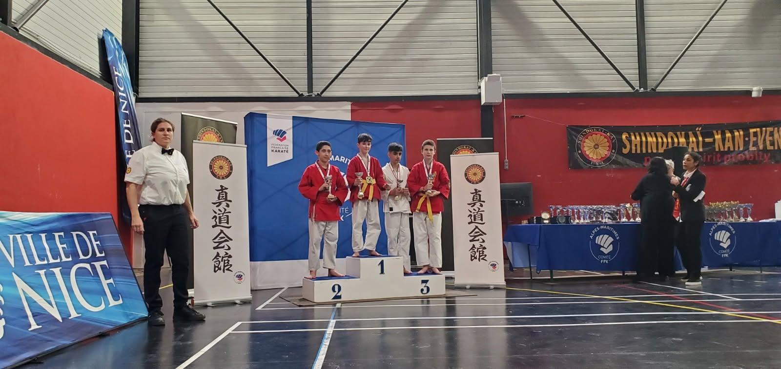 Quatre pratiquants présentent leurs médailles et leurs coupes sur un podium.